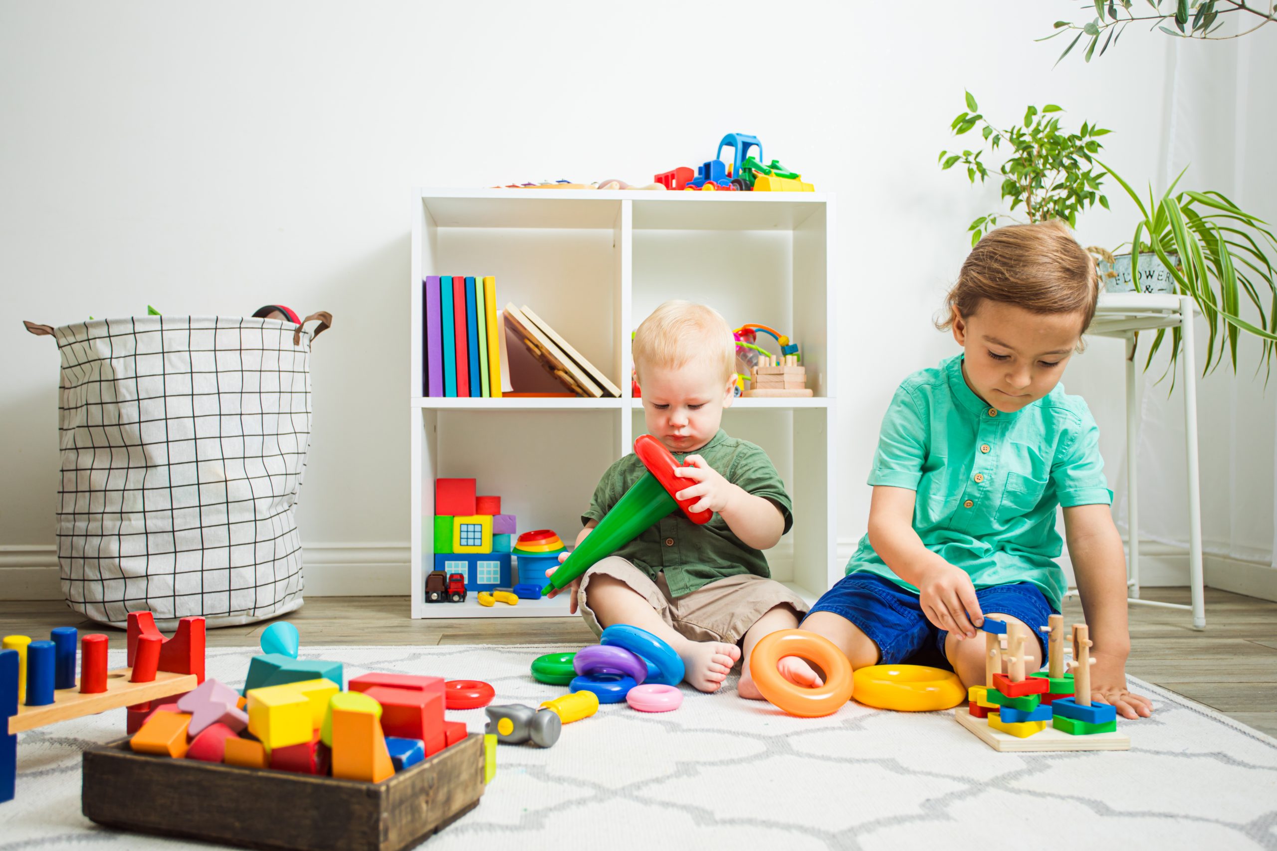 Two adorable boys playing, sitting side by side each one with own toy. Different age kids can play together peacefully. Relationship between siblings.